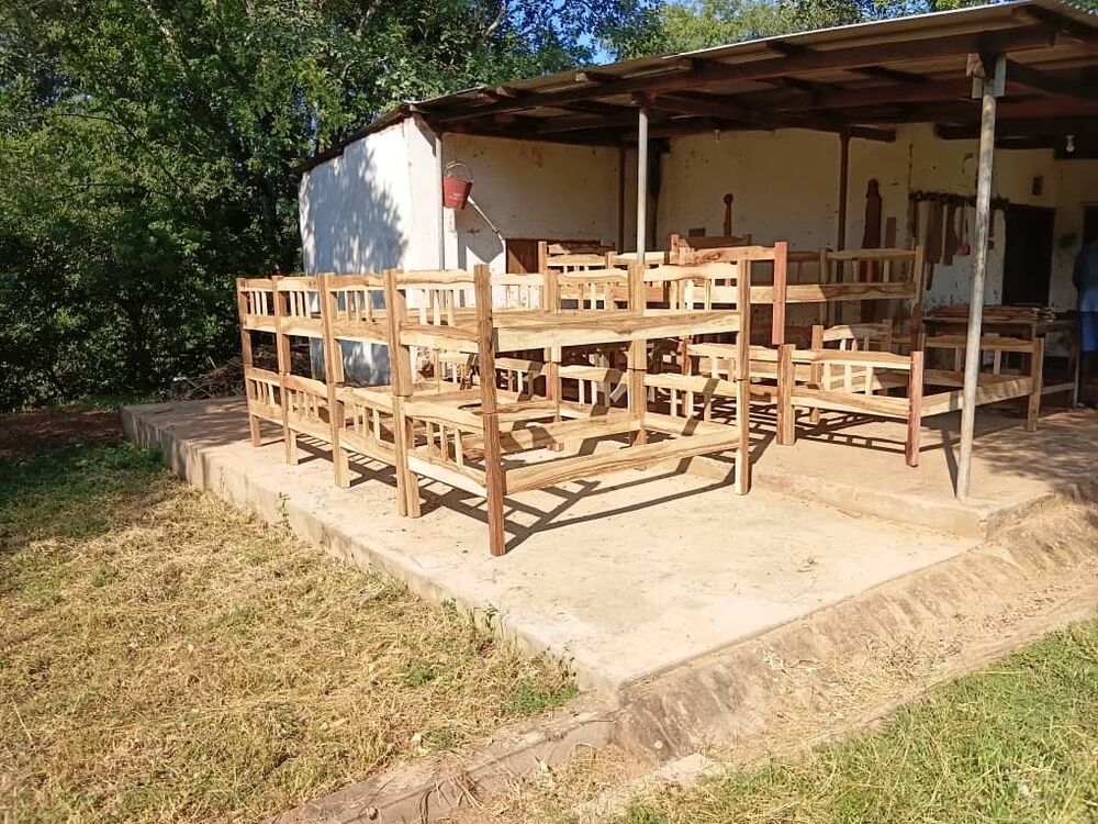 Mehrere unfertige Holz-Etagenbetten und Einzelbetten stehen unter einem einfachen Unterstand im Freien