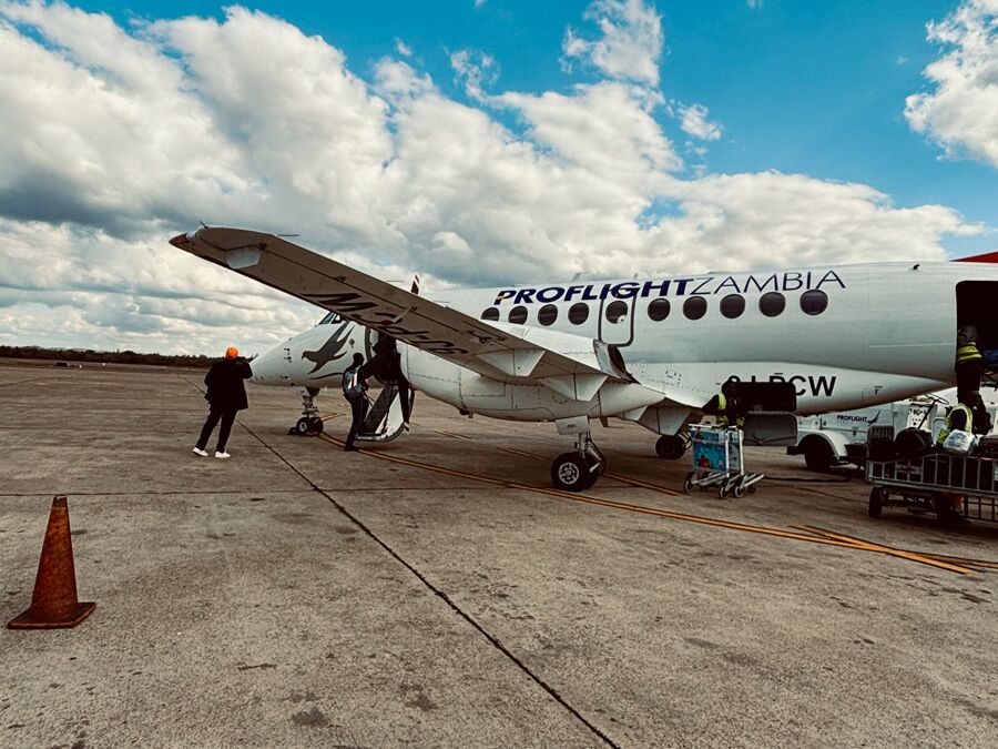Passagiere, die an einem sonnigen Tag mit verstreuten Wolken ein Flugzeug von Proflight Zambia besteigen.