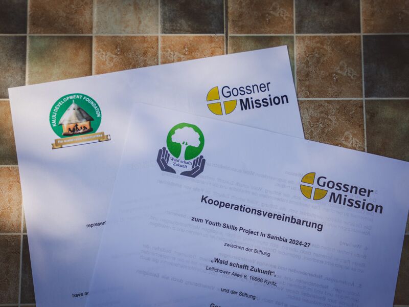 Nahaufnahme von Dokumenten auf einem Steintisch mit den Logos der Gossner Mission und einer anderen Organisation.