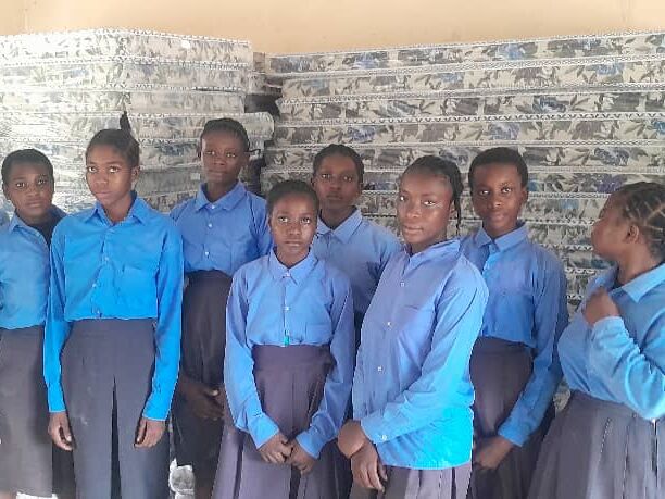 Eine Gruppe von Schülern in blauen Uniformen steht vor gestapelten Matratzen in einem Klassenzimmer