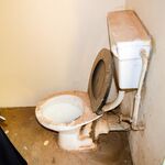 Eine alte, schmutzige Toilette in einem kleinen Raum mit beschädigten Rohren.