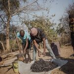 Zwei Männer zerkleinern verkohltes Pflanzenmaterial zur Brikettherstellung in Sambia