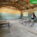 Ein verlassener, leerer Klassenraum mit beschädigten Wänden und alten Bänken. Beschriftet mit 'vorher'.