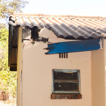 A damaged part of a building with broken roof tiles and a blue wooden beam.