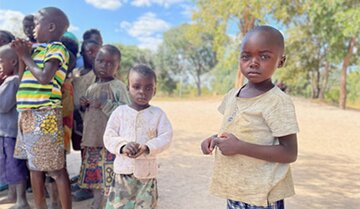 Schwarze Schulkinder mit alten Klamotten stehen unter freiem Himmel und schauen in die Kamera