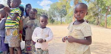 Black schoolchildren wearing old clothes stand outdoors and look into the camera