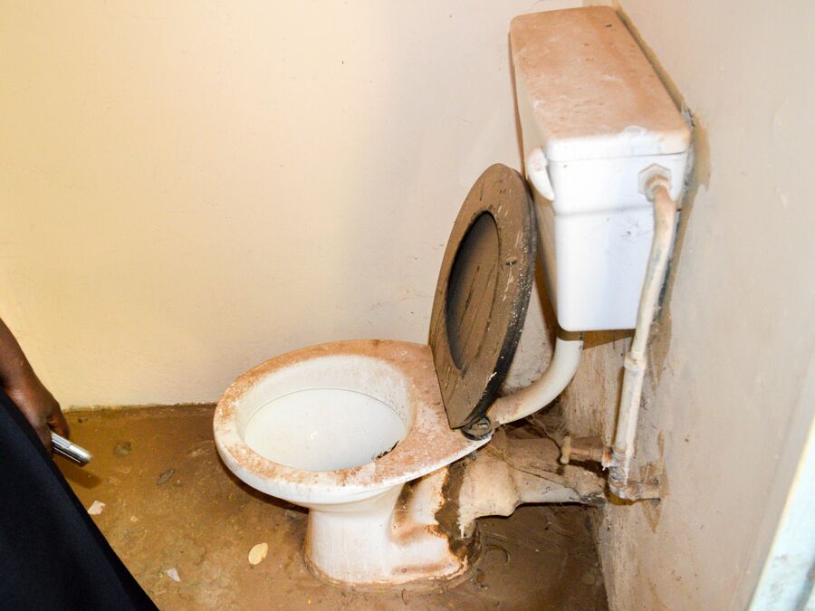 Eine alte, schmutzige Toilette in einem kleinen Raum mit beschädigten Rohren.